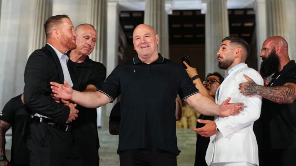 Dana White sonriente interviene en el careo entre Justin Gaethje (traje oscuro) e Ilia Topuria (traje blanco) en un evento UFC. Seguridad.