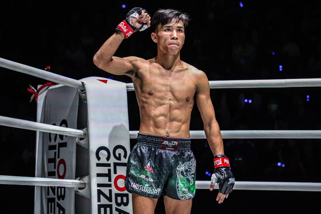 Luchador de MMA atlético con puño en alto en un ring de combate. Sin camiseta, con guantes y shorts negros con detalles verdes.