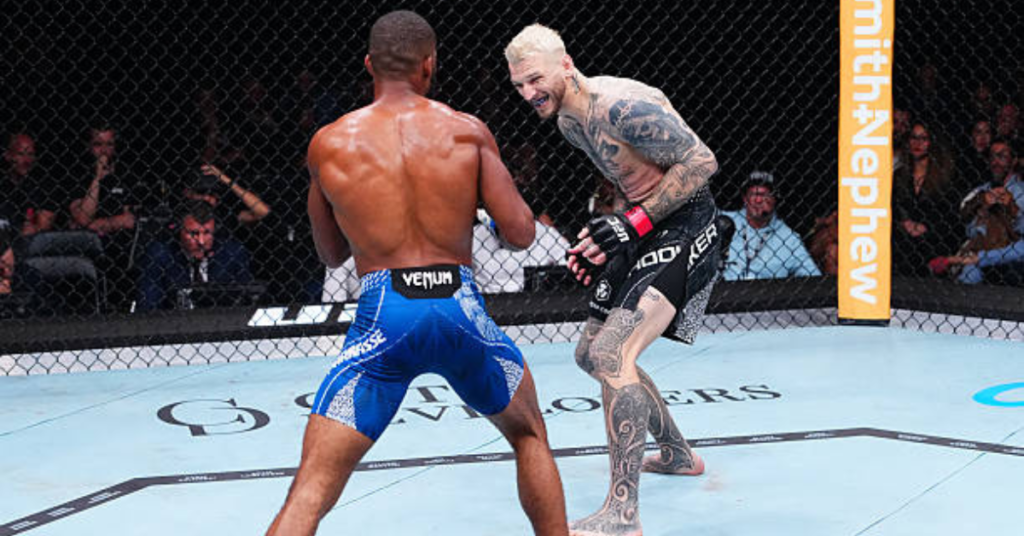 Dos luchadores de MMA en el octágono. Uno de espaldas con shorts azules, el otro, tatuado y rubio, con expresión intensa.
