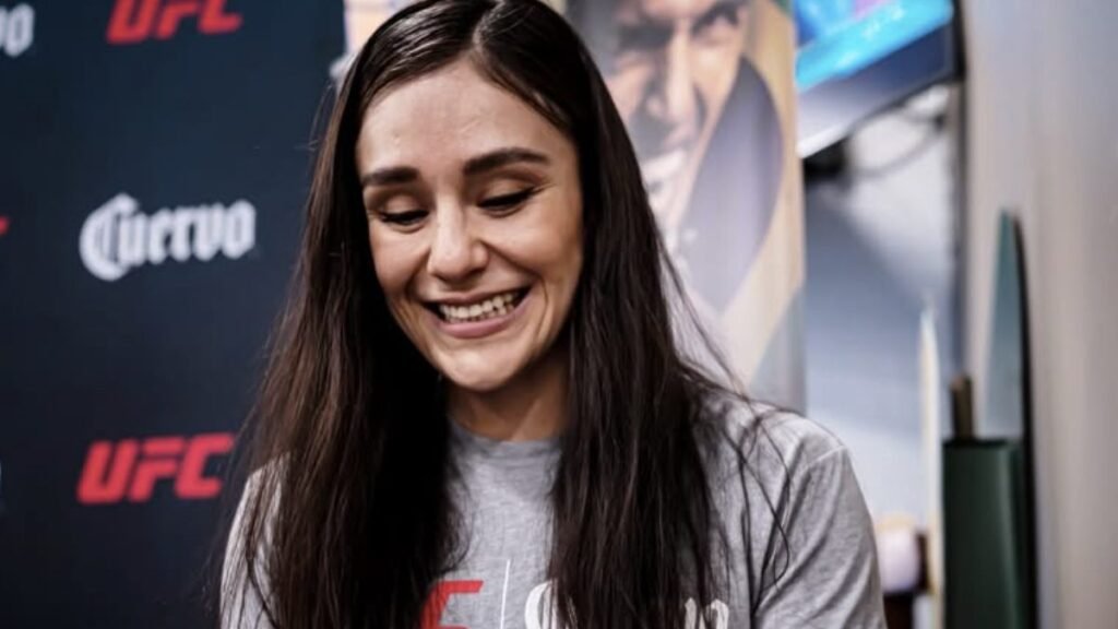 Atleta UFC sonríe con pelo oscuro y camiseta gris en un evento. Fondo con logos Cuervo y UFC.